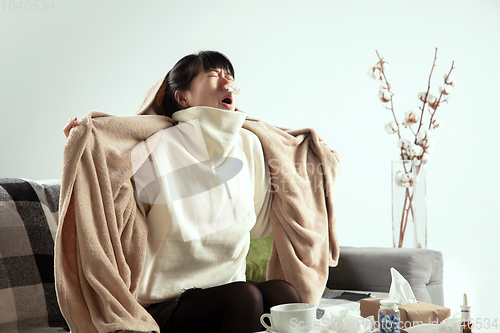 Image of Woman wrapped in a plaid looks sick, ill, sneezing and coughing sitting at home indoors