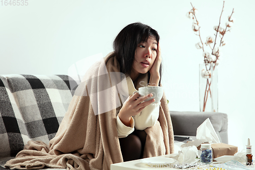 Image of Woman wrapped in a plaid looks sick, ill, sneezing and coughing sitting at home indoors