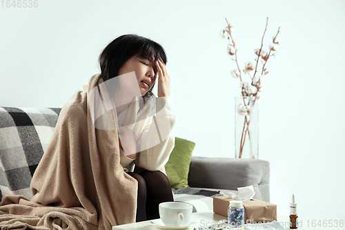 Image of Woman wrapped in a plaid looks sick, ill, sneezing and coughing sitting at home indoors