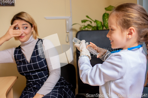 Image of Paediatrician doctor examining a child in comfortabe medical office. Little girl playing pretends like doctor for woman