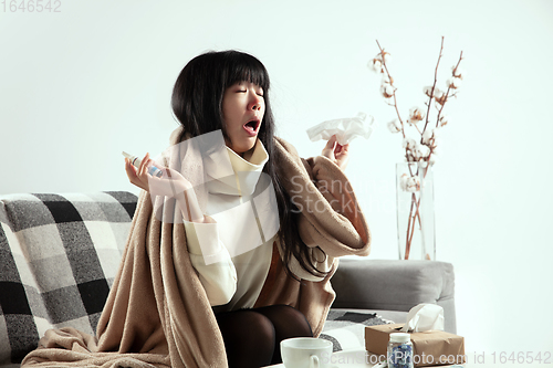 Image of Woman wrapped in a plaid looks sick, ill, sneezing and coughing sitting at home indoors