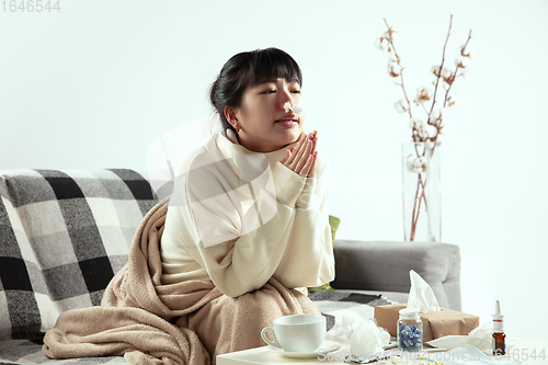 Image of Woman wrapped in a plaid looks sick, ill, sneezing and coughing sitting at home indoors