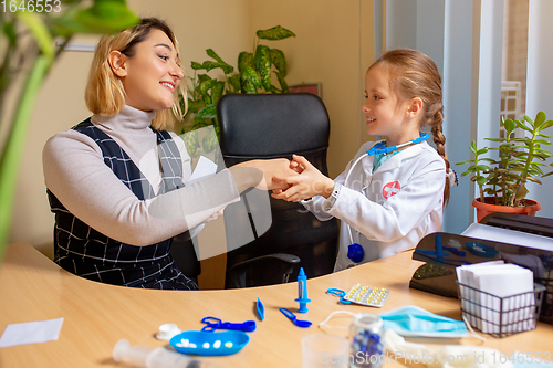 Image of Paediatrician doctor examining a child in comfortabe medical office. Little girl playing pretends like doctor for woman