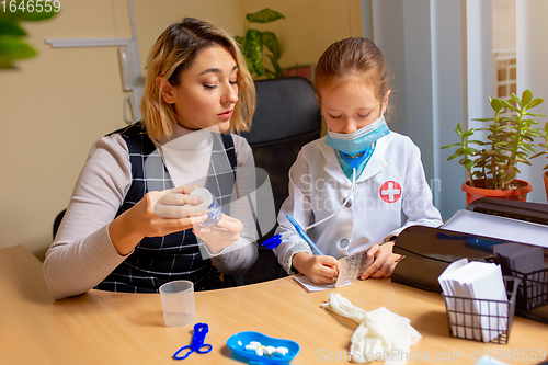 Image of Paediatrician doctor examining a child in comfortabe medical office. Little girl playing pretends like doctor for woman