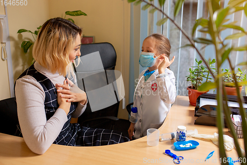 Image of Paediatrician doctor examining a child in comfortabe medical office. Little girl playing pretends like doctor for woman