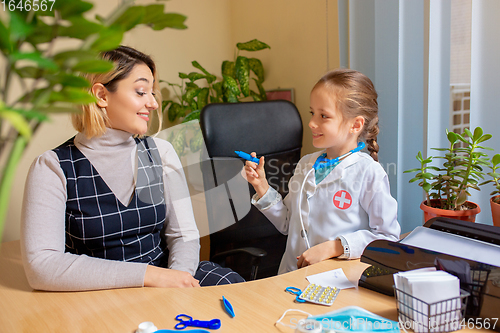 Image of Paediatrician doctor examining a child in comfortabe medical office. Little girl playing pretends like doctor for woman