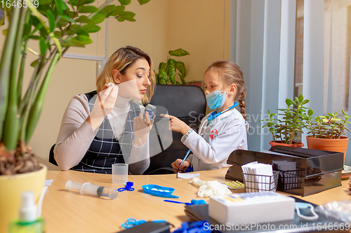 Image of Paediatrician doctor examining a child in comfortabe medical office. Little girl playing pretends like doctor for woman