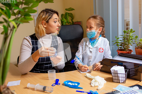 Image of Paediatrician doctor examining a child in comfortabe medical office. Little girl playing pretends like doctor for woman