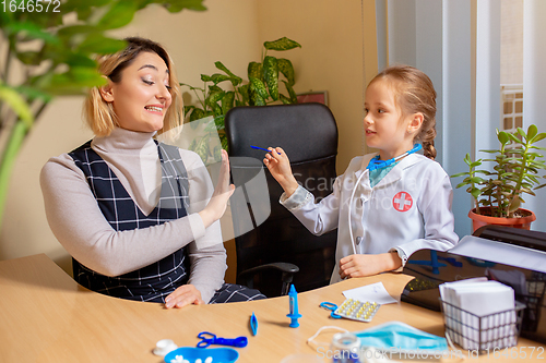 Image of Paediatrician doctor examining a child in comfortabe medical office. Little girl playing pretends like doctor for woman