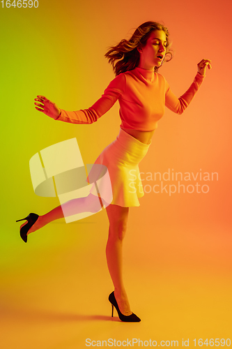 Image of Beautiful seductive girl in fashionable, romantic outfit on bright gradient green-orange background in neon light