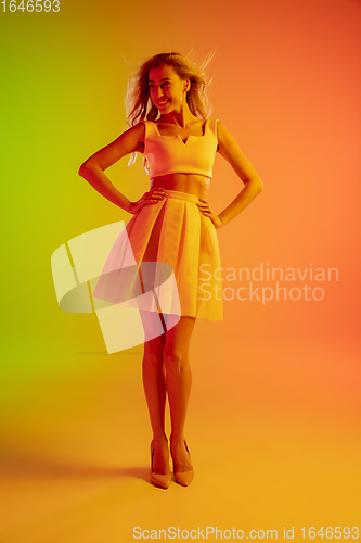 Image of Beautiful seductive girl in fashionable, romantic outfit on bright gradient green-orange background in neon light