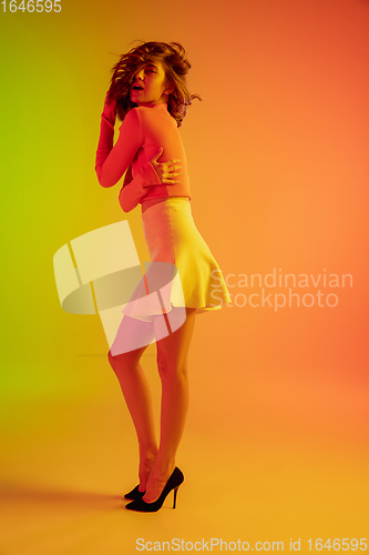 Image of Beautiful seductive girl in fashionable, romantic outfit on bright gradient green-orange background in neon light