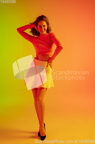 Image of Beautiful seductive girl in fashionable, romantic outfit on bright gradient green-orange background in neon light