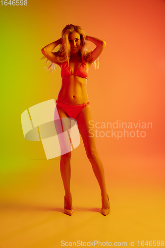 Image of Beautiful seductive girl in fashionable red swimsuit on bright gradient green-orange background in neon light