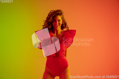 Image of Beautiful seductive girl in fashionable red swimsuit on bright gradient green-orange background in neon light