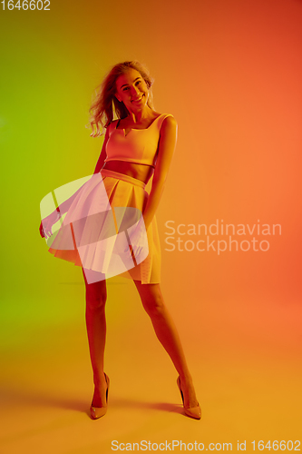 Image of Beautiful seductive girl in fashionable, romantic outfit on bright gradient green-orange background in neon light