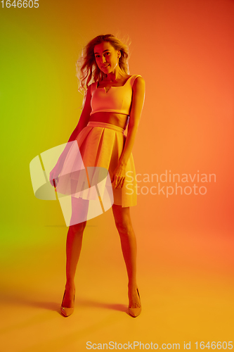 Image of Beautiful seductive girl in fashionable, romantic outfit on bright gradient green-orange background in neon light