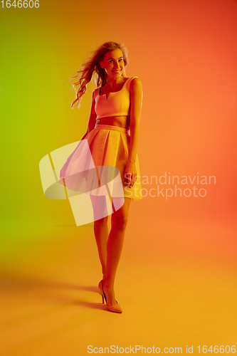 Image of Beautiful seductive girl in fashionable, romantic outfit on bright gradient green-orange background in neon light