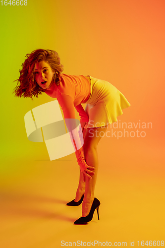 Image of Beautiful seductive girl in fashionable, romantic outfit on bright gradient green-orange background in neon light