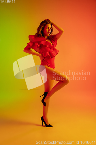 Image of Beautiful seductive girl in fashionable red swimsuit on bright gradient green-orange background in neon light