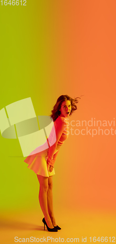 Image of Beautiful seductive girl in fashionable, romantic outfit on bright gradient green-orange background in neon light