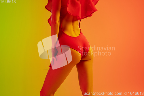 Image of Close up of beautiful seductive girl in fashionable red swimsuit on bright gradient green-orange background in neon light