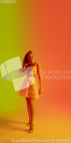 Image of Beautiful seductive girl in fashionable, romantic outfit on bright gradient green-orange background in neon light