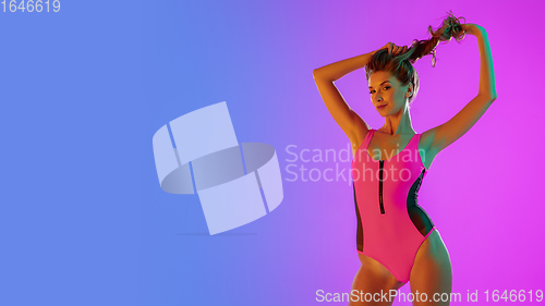 Image of Beautiful seductive girl in fashionable pink swimsuit on bright gradient purple-blue background in neon light