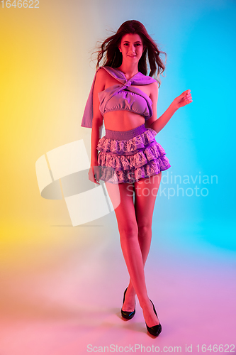 Image of Beautiful seductive girl in fashionable, romantic purple outfit on bright gradient yellow-blue background in neon light
