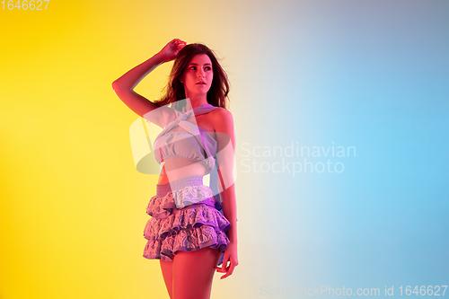 Image of Beautiful seductive girl in fashionable, romantic purple outfit on bright gradient yellow-blue background in neon light