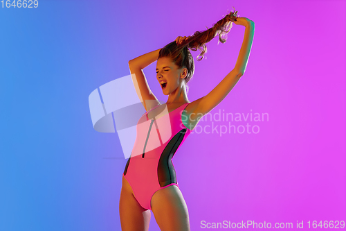 Image of Beautiful seductive girl in fashionable pink swimsuit on bright gradient purple-blue background in neon light