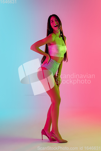 Image of Beautiful seductive girl in fashionable swimsuit on bright gradient pink-blue background in neon light