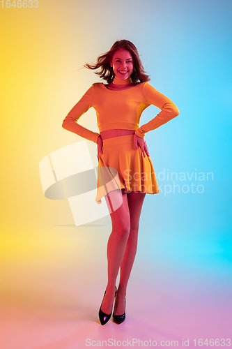 Image of Beautiful seductive girl in fashionable, romantic yellow outfit on bright gradient yellow-blue background in neon light