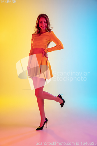 Image of Beautiful seductive girl in fashionable, romantic yellow outfit on bright gradient yellow-blue background in neon light
