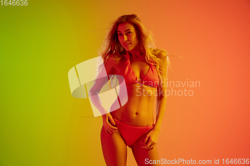 Image of Beautiful seductive girl in fashionable red swimsuit on bright gradient green-orange background in neon light
