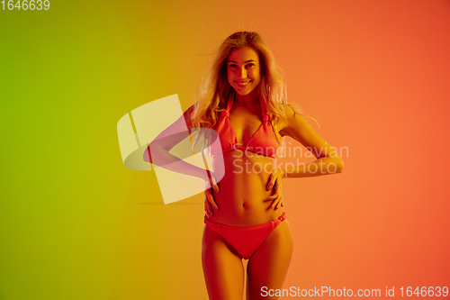 Image of Beautiful seductive girl in fashionable red swimsuit on bright gradient green-orange background in neon light