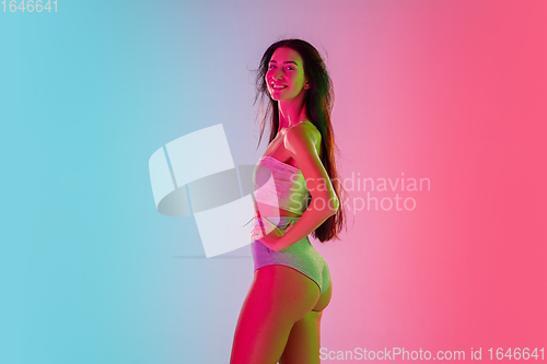 Image of Beautiful seductive girl in fashionable swimsuit on bright gradient pink-blue background in neon light