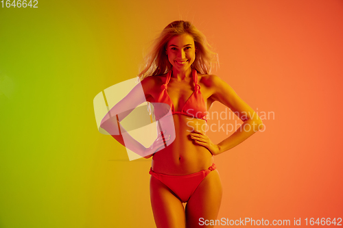 Image of Beautiful seductive girl in fashionable red swimsuit on bright gradient green-orange background in neon light