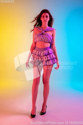 Image of Beautiful seductive girl in fashionable, romantic purple outfit on bright gradient yellow-blue background in neon light