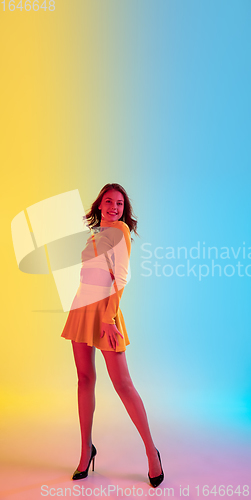 Image of Beautiful seductive girl in fashionable, romantic yellow outfit on bright gradient yellow-blue background in neon light