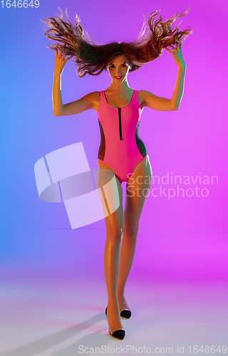 Image of Beautiful seductive girl in fashionable pink swimsuit on bright gradient purple-blue background in neon light