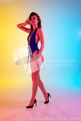 Image of Beautiful seductive girl in fashionable blue swimsuit on bright gradient yellow-blue background in neon light