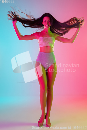 Image of Beautiful seductive girl in fashionable swimsuit on bright gradient pink-blue background in neon light