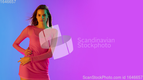 Image of Beautiful seductive girl in fashionable, romantic pink outfit on bright gradient purple-blue background in neon light