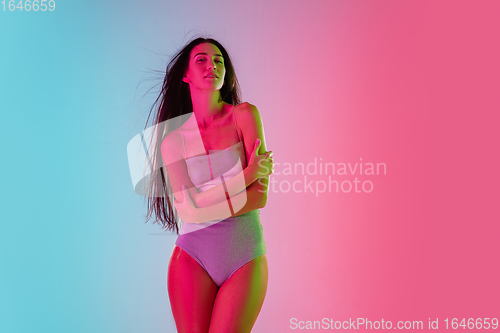Image of Beautiful seductive girl in fashionable swimsuit on bright gradient pink-blue background in neon light
