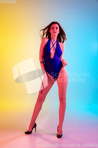 Image of Beautiful seductive girl in fashionable blue swimsuit on bright gradient yellow-blue background in neon light