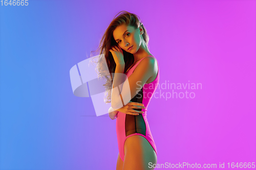 Image of Beautiful seductive girl in fashionable pink swimsuit on bright gradient purple-blue background in neon light