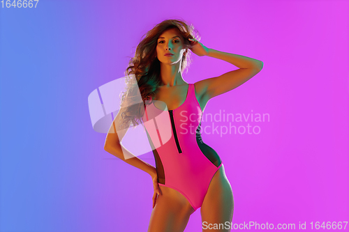 Image of Beautiful seductive girl in fashionable pink swimsuit on bright gradient purple-blue background in neon light