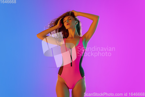 Image of Beautiful seductive girl in fashionable pink swimsuit on bright gradient purple-blue background in neon light