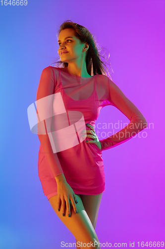 Image of Beautiful seductive girl in fashionable, romantic pink outfit on bright gradient purple-blue background in neon light